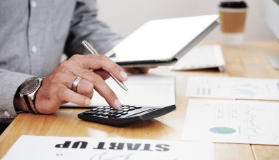Close-up of businessman counting the profit of the company and using digital tablet at office desk
